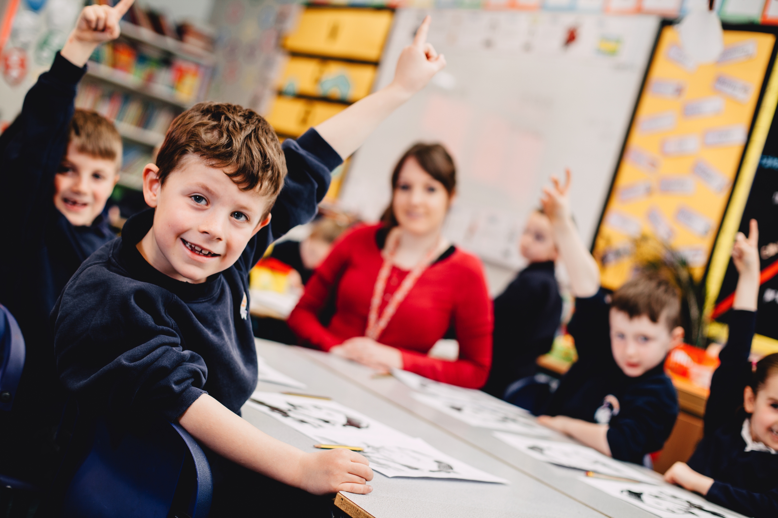 Pupils in a classroom holding their hands up