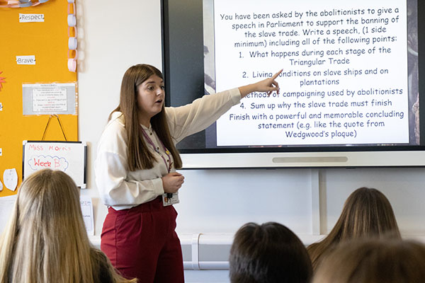 A secondary school teacher pointing to some text on the board